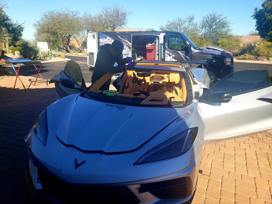 Technician installing a new windshield on a Corvette C8 in the customer's driveway with the Perfect Touch van on site