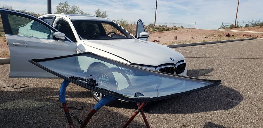 New windshield staged on a stand in front of the customer's BMW, doors open and ready for install