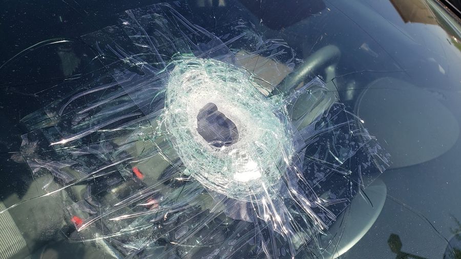 Close-up of a large windshield impact with spreading cracks, taped for safe driving before replacement